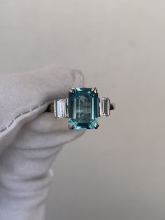 an emerald and diamond ring sitting on top of a white glove