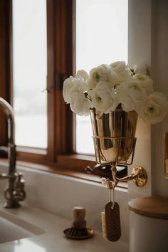 a vase with white flowers in it sitting on a counter next to a sink and window