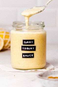 a jar filled with curry and yogurt sauce on top of a table next to sliced lemons