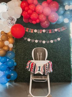 a baby's high chair in front of a backdrop with balloons and streamers