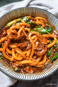 a bowl filled with beef and noodles on top of a white table cloth next to a fork