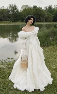 a woman in a white dress standing next to a lake