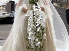 the bride is walking down the street in her wedding dress and holding a bouquet of white flowers