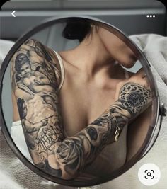 a woman with tattoos on her arm looking in a mirror and holding onto the camera