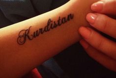 a person with a tattoo on their arm that reads, kurdistan in cursive writing