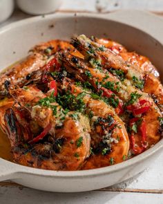 a white bowl filled with shrimp covered in sauce and garnished with parsley