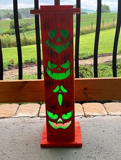 a red wooden sign with green faces painted on it's sides and a fence in the background