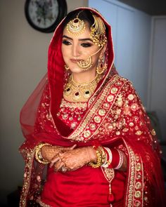 a woman wearing a red and gold bridal outfit with her hands on her hips