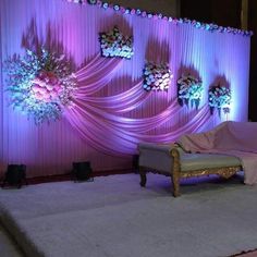 a stage set up for a wedding with flowers on the wall and draping