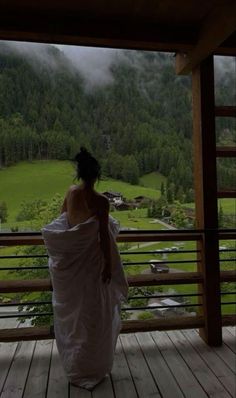 a woman in a white dress is standing on a porch looking out at the mountains