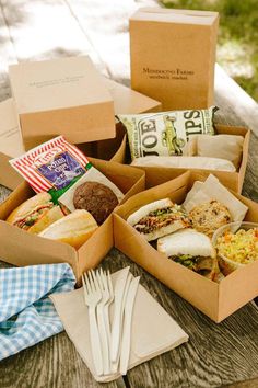 an open box filled with food sitting on top of a wooden table next to utensils and napkins