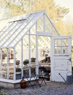 a small white greenhouse sitting on top of a brick patio next to a building with windows