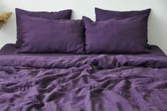 a bed with purple sheets and pillows on top of it next to a teddy bear