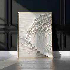 an abstract white painting in a gold frame on the floor next to a black wall