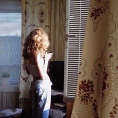 a woman standing in front of a window with her back to the camera and looking out