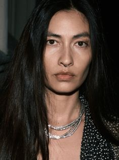 a woman with long black hair and necklaces on her neck looking at the camera