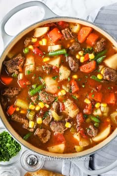 a pot filled with stew and vegetables on top of a white table next to bread