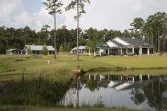 a large house sitting on top of a lush green field next to a lake in front of a forest