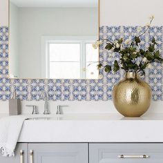 a gold vase filled with flowers sitting on top of a bathroom counter next to a mirror