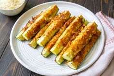 several pieces of zucchini on a white plate next to a bowl of grated parmesan cheese