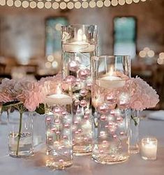 the centerpieces are filled with pink flowers and lit candles in glass vases