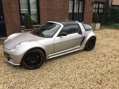 a silver sports car parked in front of a brick building next to a gravel driveway