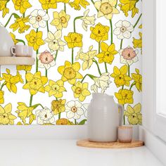 yellow and white flowers are on the wall next to a vase with a cup in it