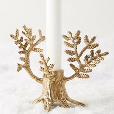 a white candle with some gold leaves on it and a tree branch in the middle