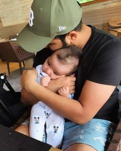 a man holding a baby in his arms while sitting next to another person with a hat on