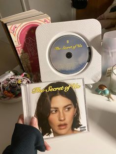 a person holding up a cd in front of a table with other items on it