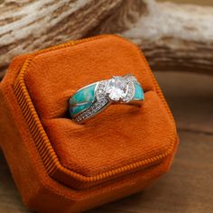 a diamond and turquoise ring sits in an orange velvet box on top of a piece of wood