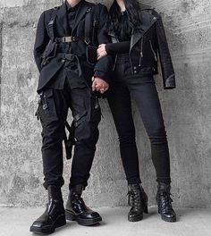 two people standing next to each other in black clothes and boots, one holding the hand of another person's shoulder