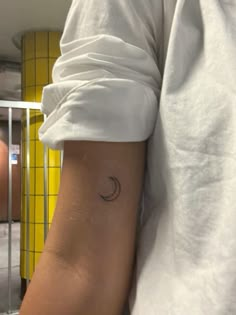 a person wearing a white shirt with a small crescent tattoo on their left side arm