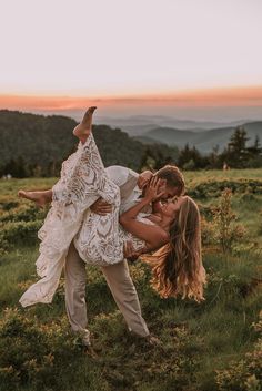 a couple kissing in the middle of a field with mountains in the background at sunset