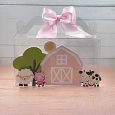 a clear box with two farm animals and a pink bow on the top, sitting on a wooden table