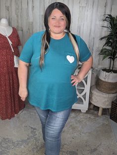 Get ready to feel comfy and cute in the Kensie Teal Flowy Tee! Made with a soft fleece material, its somehow the softest thing ever without being heavy or hot! so good! The beautiful dark teal color is complemented by a white heart graphic on the chest pocket. With elbow length sleeves and stretch throughout, this tee is perfect for pairing with your favorite leggings, jeans, or skirt. Spread happy vibes in this playful and versatile top. Fit: Relaxed. Michele is a size 20, apple shaped, wearing Dark Teal Color, Layering Hoodies, Favorite Leggings, Heart Pocket, Apple Shaped, Plus Size Boutique, Sweater Layering, Heart Graphic, Long Tank