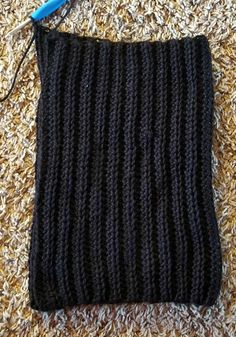 a crocheted black bag sitting on top of a carpet next to a blue knitting needle