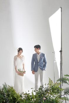 a man and woman standing next to each other in front of greenery with one holding a bouquet