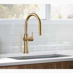 a gold faucet on a white counter top in a kitchen with tile backsplash