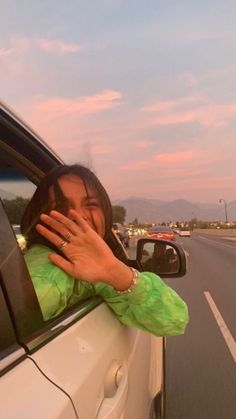 a woman leaning out the window of a car with her hand up to her face