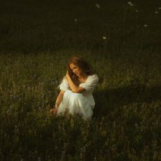 a woman in a white dress sitting on the ground with her hands behind her head