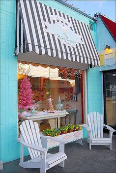 two white adiron chairs sitting in front of a blue building with black and white striped awning