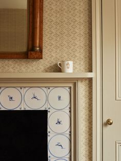 a white fireplace with blue and white tiles on it's mantle next to a mirror