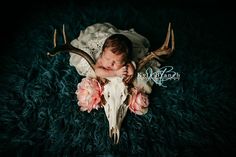 a baby is sleeping in a deer skull with pink flowers on it's head