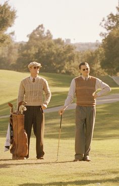 two men standing next to each other holding golf clubs