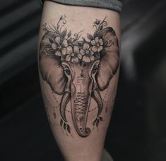 an elephant with flowers on it's head is sitting next to a woman's leg