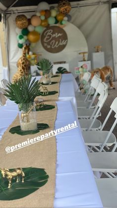 the table is set up for a baby shower with giraffes and palm leaves