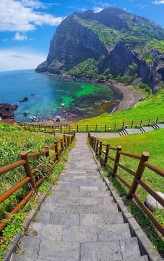 stairs lead down to the beach with green hills in the background and blue water on either side