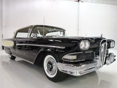 an old black car is parked in a white room with no one around it,