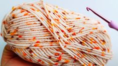 a ball of white yarn with orange and yellow sprinkles next to a crochet hook